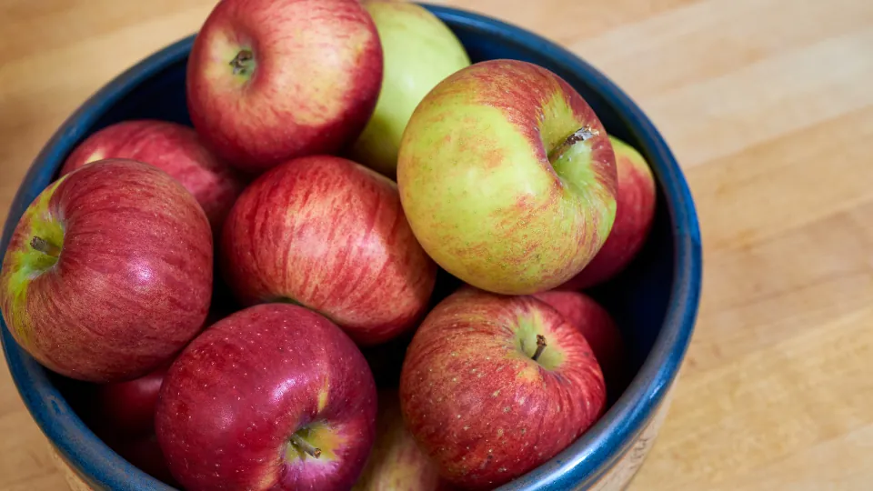 Un cuenco azul lleno de manzanas rojas y verdosas sobre una superficie de madera.