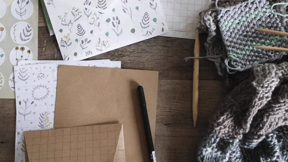 Una mesa de trabajo con labor de punto, tijeras y un patrón sobre tela.