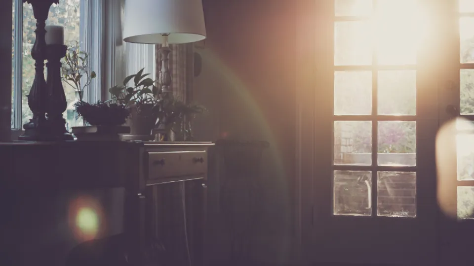 Una habitación en penumbra con la luz del atardecer entrando por la ventana.