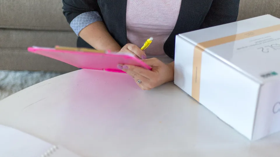 Manos sosteniendo una carpeta y una hoja con anotaciones sobre una mesa.