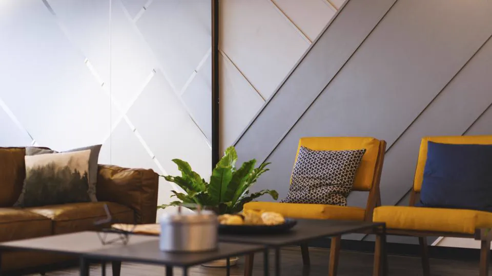 Una sala con sofá, sillones, mesas bajas, una planta y decoración geométrica en la pared.
