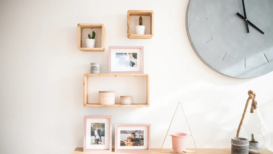 Una pared con estanterías de madera, marcos de fotos y un reloj.