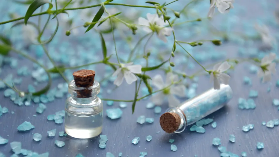Un frasco de aceite esencial entre flores blancas y cuentas azules.