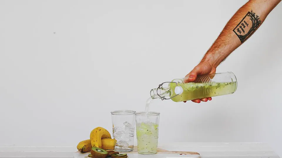 Un brazo sirve una bebida fresca de una botella a un vaso, junto a limones.