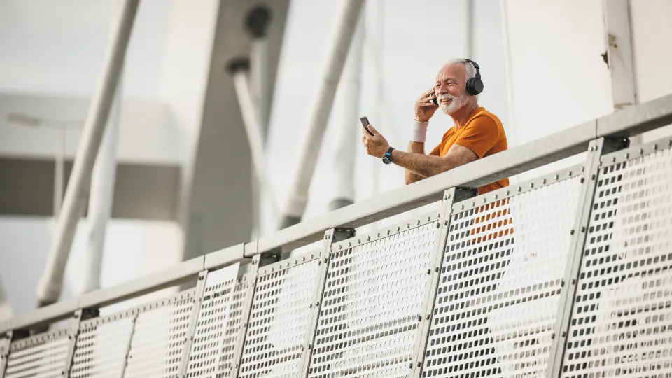 Un hombre mayor con camisa naranja camina por un paseo exterior luminoso.