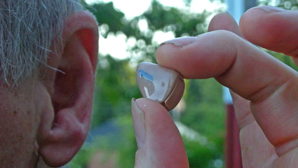Una mano coloca un audífono en la oreja de una persona mayor.