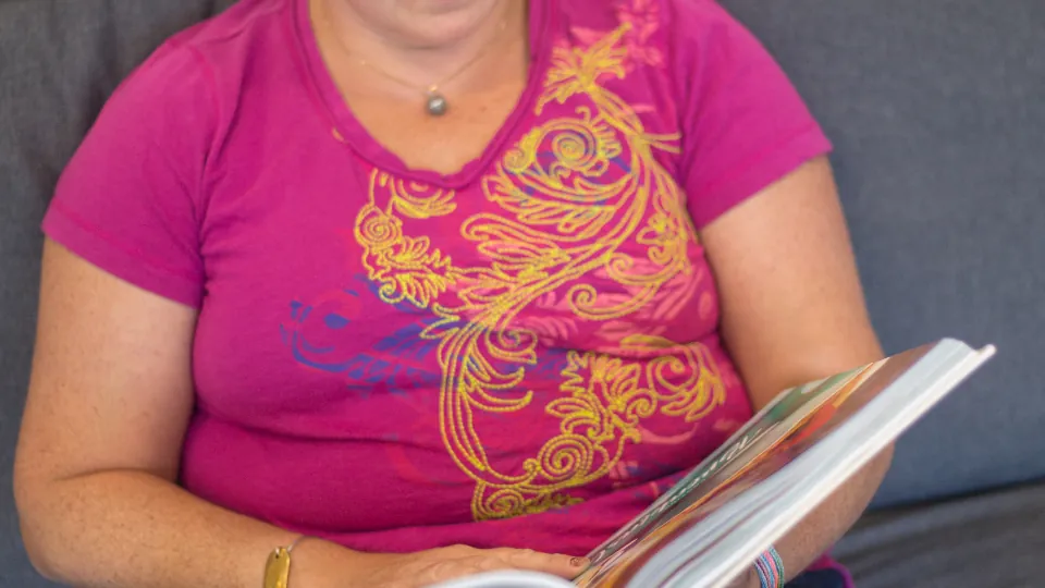 Una mujer mayor lee sentada en un sofá durante su recuperación en casa.