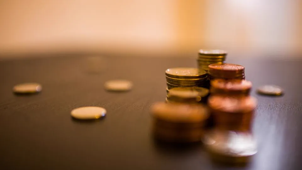 Varias monedas doradas sobre una mesa oscura; algunas están apiladas y otras dispersas.