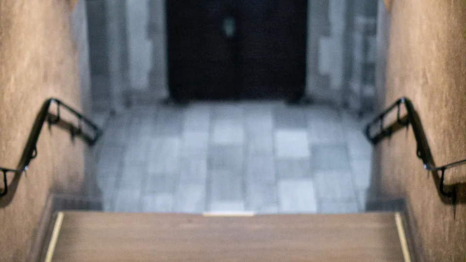 Una escalera interior desciende entre pasamanos a ambos lados, con una puerta oscura al fondo.